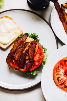 there is a plate with a sandwich on it and bacon in the middle, along with two slices of tomato