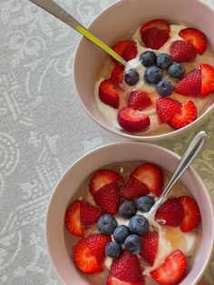 two bowls of yogurt with strawberries and blueberries in them on a table