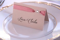 a place card with a pink bow on it sitting on top of a white plate