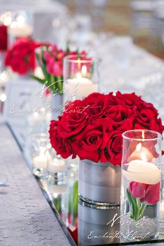 red roses and candles sit in glass vases on a long table with silverware