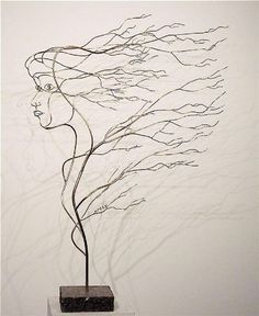 a metal sculpture with a woman's head on top of it and branches blowing in the wind