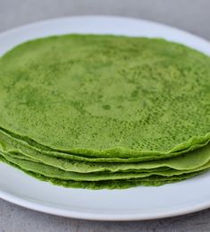 three green pancakes on a white plate sitting on a gray counter top, ready to be eaten