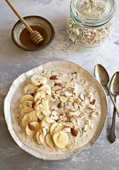 a bowl of oatmeal with bananas and nuts next to a jar of honey