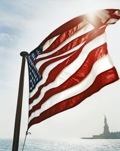 an american flag flying in front of the statue of liberty