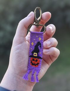 a hand holding a purple keychain with a pumpkin on it