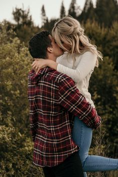 a man and woman kissing in front of trees