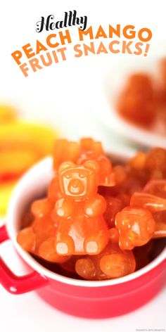 a bowl filled with orange gummy bears sitting on top of a white table next to bananas