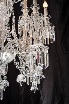 a crystal chandelier hanging from the ceiling with two candles in it and one light turned on