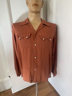 1940s/1950s rust brown gabardine western shirt with a loop collar, mother of pearl snap buttons and two double pointed flap pockets. 3 buttons on the cuffs. Made by American label Fleetline.Great condition with the exception of a small discolouration on the lower left side of the front (see last photo) Measurements  Shoulders 19 inches  Pit to pit 24 inches  Length 27 inches  Sleeves 24 inches  All items sold as seen. Please contact seller for more details and offers Western Brown Collared Tops, Western Style Brown Collared Top, Western Style Brown Tops With Buttons, Western Brown Tops With Buttons, Brown Western Style Top With Buttons, Brown Western Top With Buttons, Western Brown Tops With Snap Buttons, Brown Collared Western Shirt, Brown Shirt With Lapel Collar And Button Closure