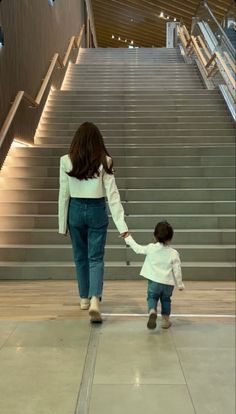 a woman holding the hand of a small child walking down stairs in front of an escalator