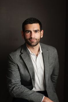 a man in a gray jacket and white shirt is posing for the camera with his arms crossed