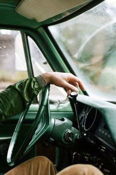 a man sitting in the driver's seat of a green truck with his hand on the steering wheel