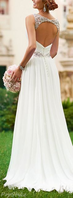 a woman in a wedding dress standing on the grass with her back to the camera