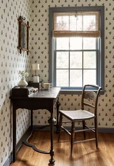 a desk and chair in front of a window with wallpapered walls behind it