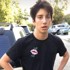 a young man standing in front of a parked car with his hands on his hips