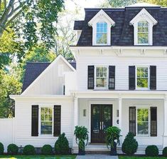 a large white house with black shutters on the front and side windows, surrounded by trees