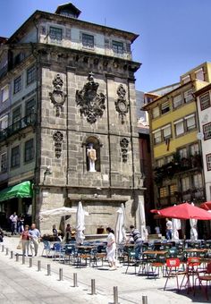 an old building with tables and umbrellas in front of it on a city street