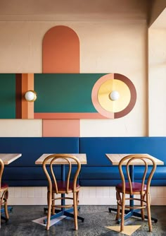 three wooden chairs sitting in front of a blue booth with white tables and two lamps hanging from the ceiling