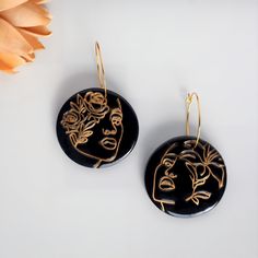 "READY TO SHIP:  Gold Line Feminine Face Image Earrings on Glossy Black. HYPOALLERGENIC EAR WIRES: Gold-colored stainless steel hoop ear wires for both comfort and style. SLEEK AND SPARKLING: Sleek round glossy black earrings with a subtle hint of sparkle. Each earring features a unique gold line face accented with flowers. Simple, clean, and beautiful. DIMENSIONS: Approximately 2 inches in length (1.25\" earring base hanging from 1\" hoop) and approximately 1.5 inches in width. LIGHTWEIGHT AND DURABLE: Crafted from lightweight and durable polymer clay, coupled with surgical stainless steel (considered hypoallergenic and rust/tarnish-resistant) ear wires, making these earrings ideal for daily wear. FASHIONABLE VERSATILITY: Suitable for a variety of occasions, from formal wear to casual out Simple Line Art, Feminine Face, Face Jewelry, Line Art Woman, Flowers Simple, Face Jewellery, Polymer Earrings, Face Earrings, Art Earrings