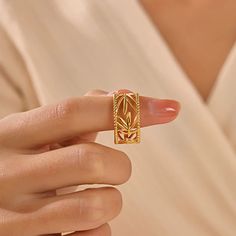 a woman's hand holding a gold ring with leaves on the front and sides