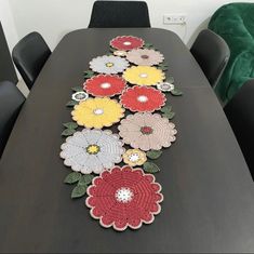 a long table with crocheted flowers on it and black chairs around the table