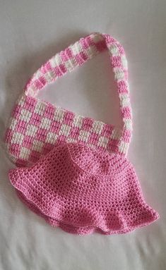 a crocheted pink and white purse sitting on top of a bed next to a pillow