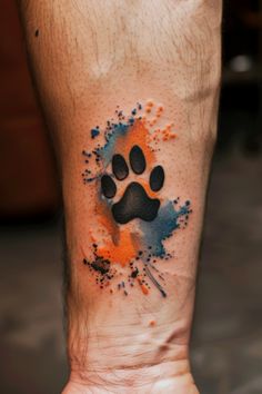 a person with a paw tattoo on their arm and hand is holding an orange and blue ink splattered paw