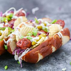 two hot dogs covered in toppings sitting on top of a table next to chips