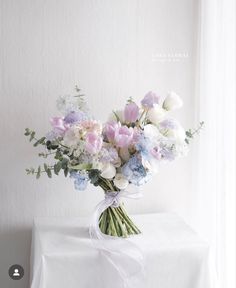 a bouquet of flowers sitting on top of a table next to a white curtain and window