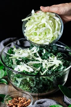 someone is adding chopped lettuce to a salad in a glass bowl on top of a wooden table