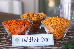 three bowls filled with different types of food on top of a table next to a sign that says goldfish bar