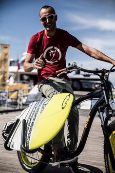 a man sitting on top of a bike holding a surfboard