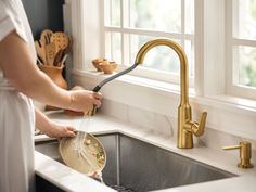 a woman washing dishes in a kitchen sink with a gold faucet and strainer