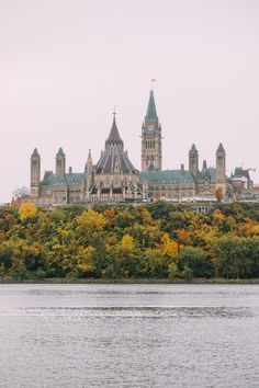 a large building sitting on top of a hill next to a body of water with trees in front of it