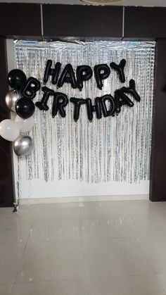 a happy birthday sign with balloons and streamers on the wall in front of it