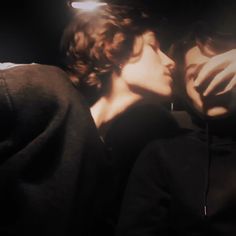 two people are kissing in the dark, one is wearing a hoodie and the other wears a sweatshirt