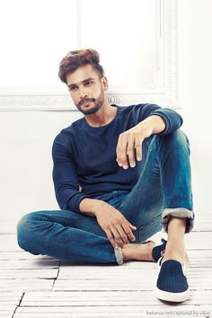 a man sitting on the floor with his legs crossed and looking at the camera while wearing blue jeans