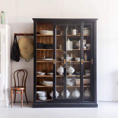 an old china cabinet with glass doors and dishes on it's shelves next to a chair