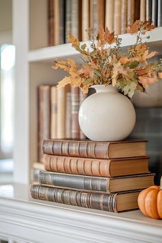 a white vase filled with flowers sitting on top of two books next to a pumpkin