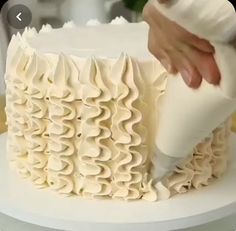 a person is decorating a cake with white icing and ruffles on it