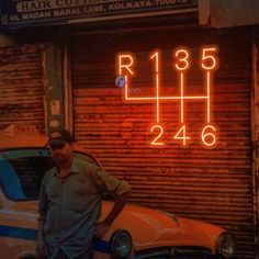 a man standing next to a parked car in front of a building with neon numbers on it