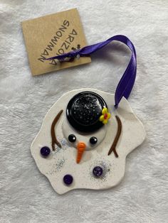 a snowman ornament with a purple ribbon around it on a white surface