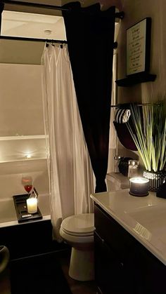 a white toilet sitting next to a bath tub in a bathroom under a black shower curtain