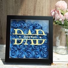 a blue rosette frame with the word dad on it and some pink flowers in a vase