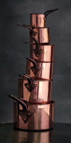 a stack of copper pots sitting on top of each other in front of a black wall