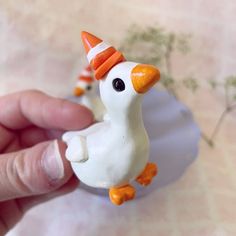 a hand holding a small toy duck with an orange and white hat