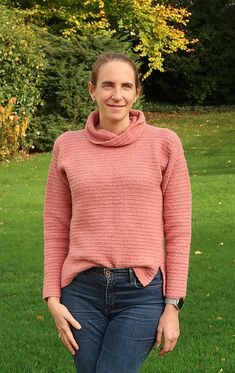 a woman standing in the grass with her hands on her hips wearing a pink sweater and jeans