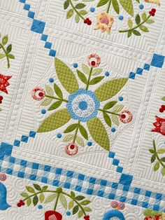 a close up of a quilt with flowers and leaves on the front, along with blue trimmings