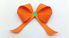 an orange paper bow with a green button on the end, sitting on a white surface