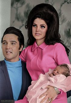 a man holding a baby next to a woman in a pink dress and blue sweater